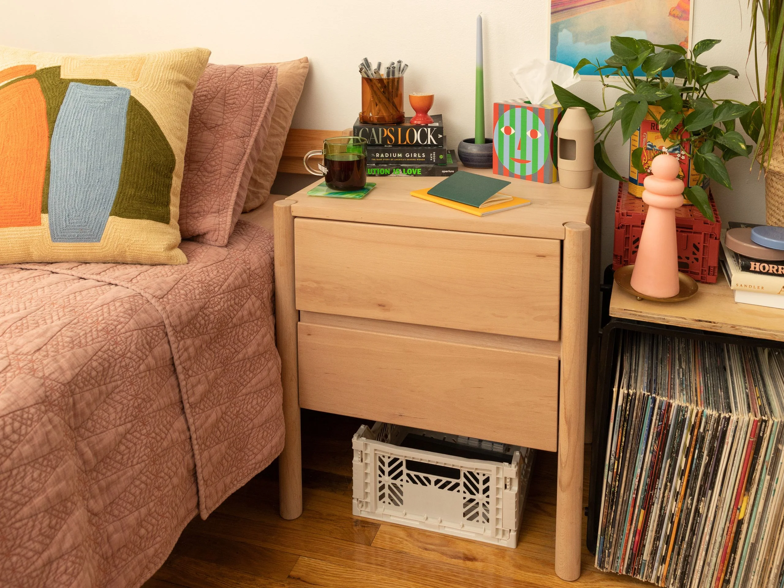 Light wood nightstand next to a bed with a pink quilt