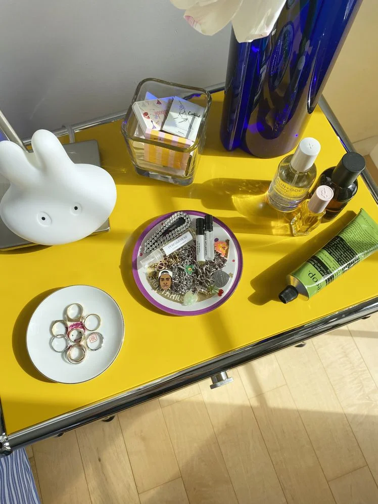 Yellow and silver nightstand styled with a lamp, vase of flowers, and assorted trinkets.