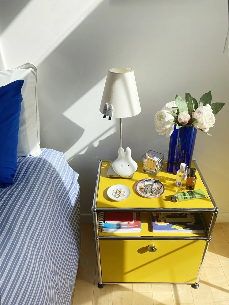  USM Haller P bright yellow bedside table styled with lamp and blue vase of white flowers