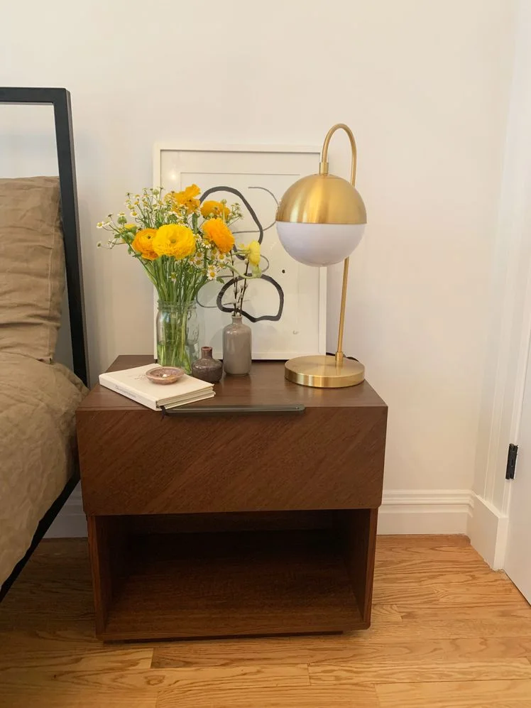 Article Nera Nightstand styled with a gold lamp, vase of yellow flowers, and notebook.