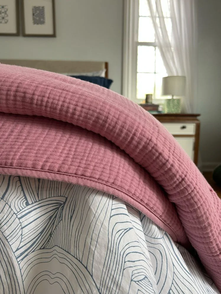 Pink quilt draped over the edge of a bed.